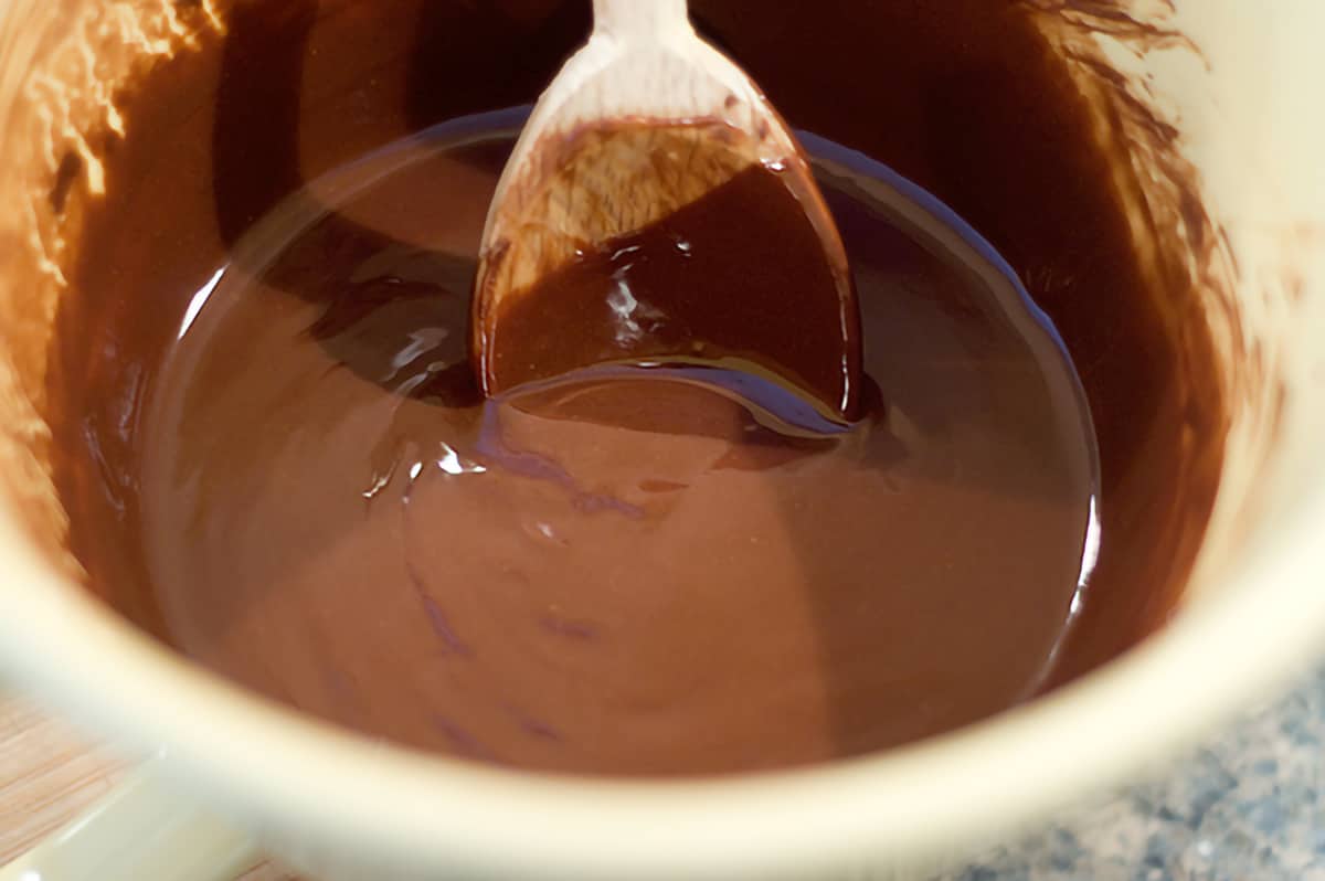 Melted chocolate and butter in a mixing bowl with a wooden spoon.