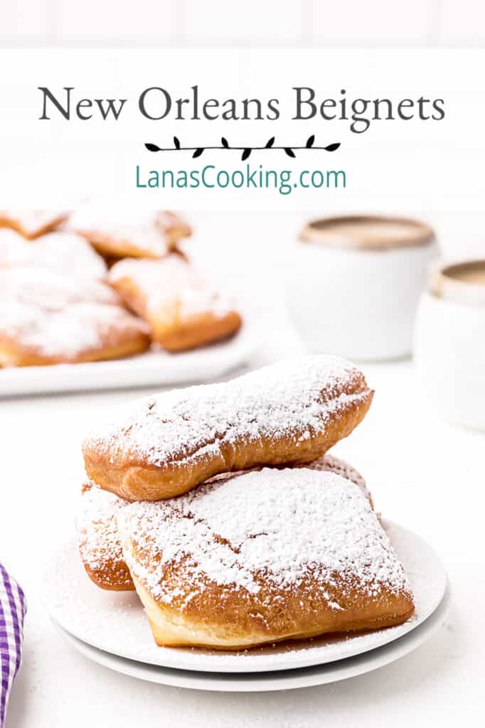 A serving of beignets topped with powdered sugar with a cafe au lait in the background.