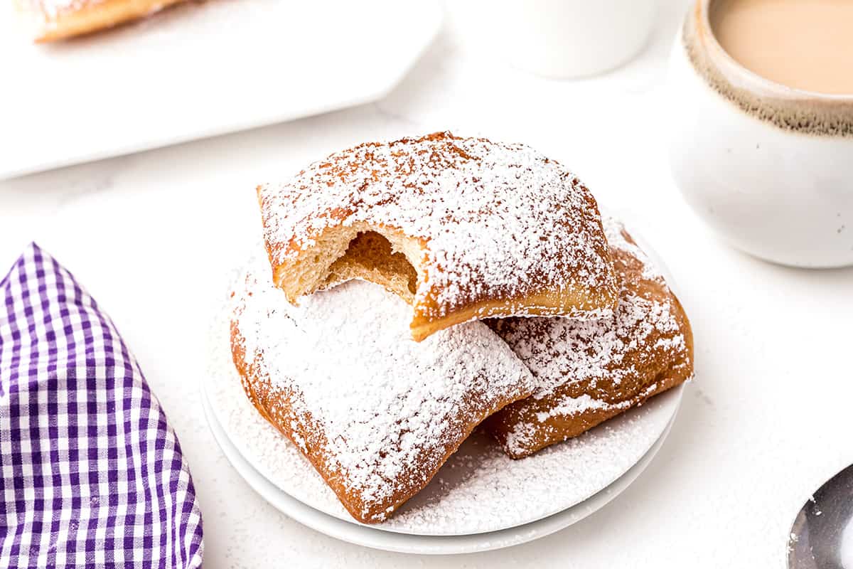 A serving of beignets topped with powdered sugar with cafe au lait to the side.