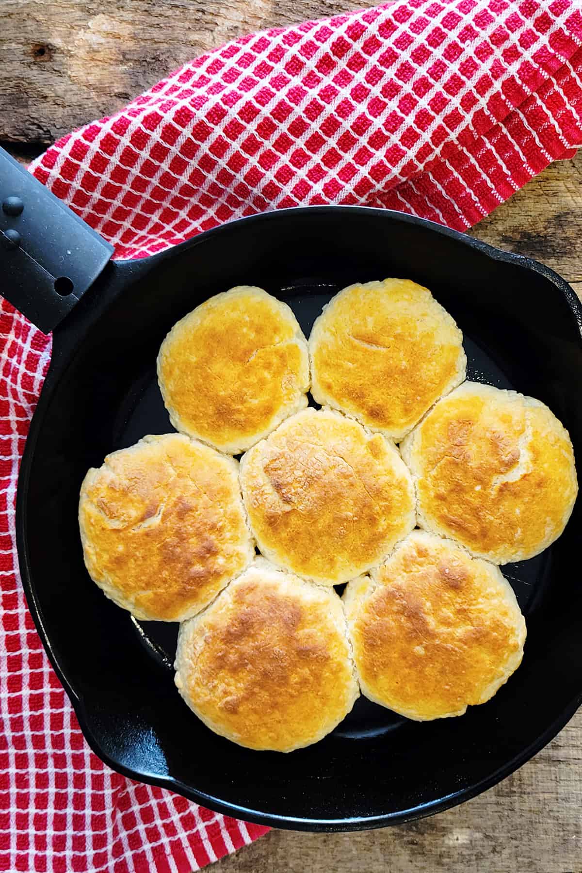 Baked buttermilk biscuits in a cast iron skillet on a wooden board.