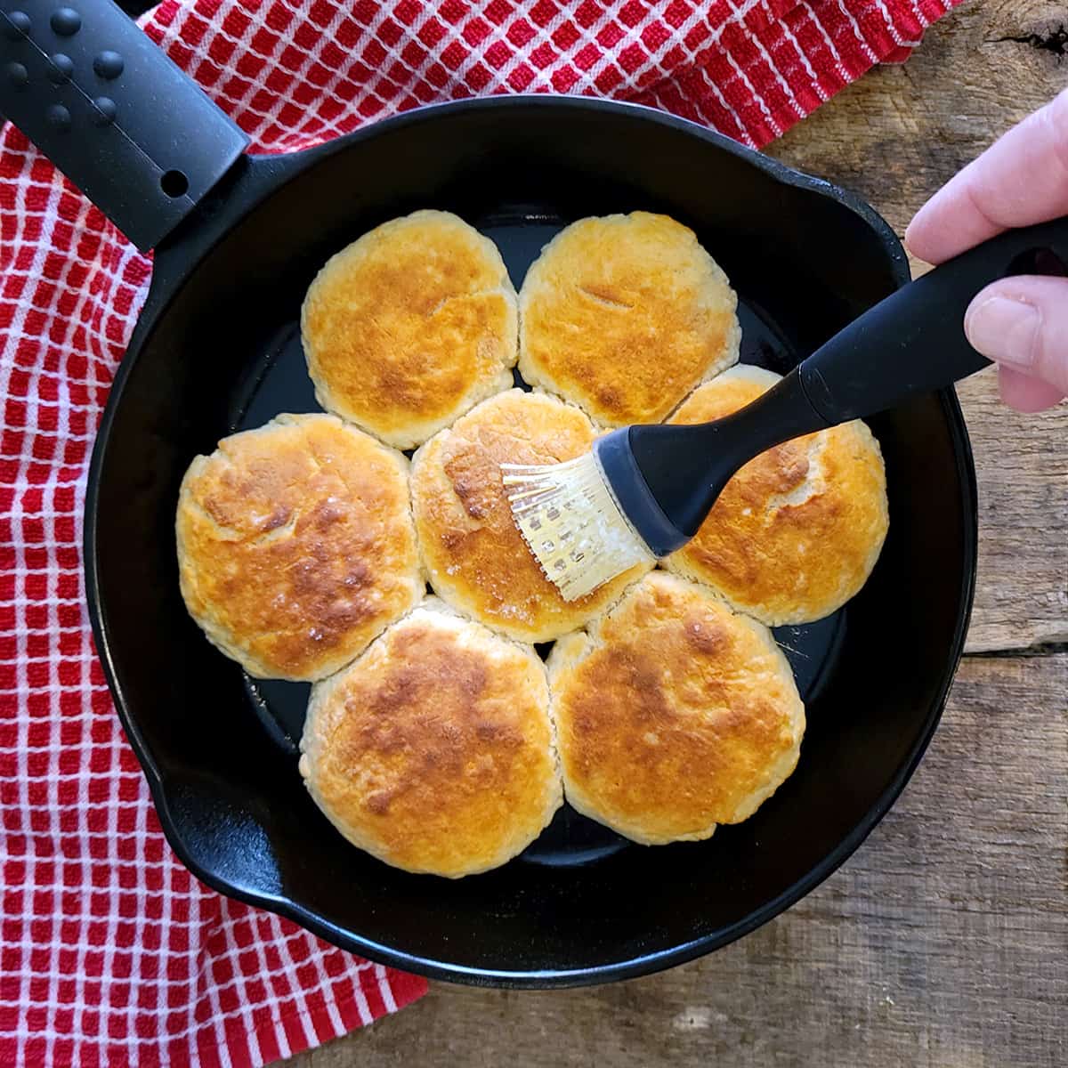 Basting baked biscuits with butter in a cast iron skillet.