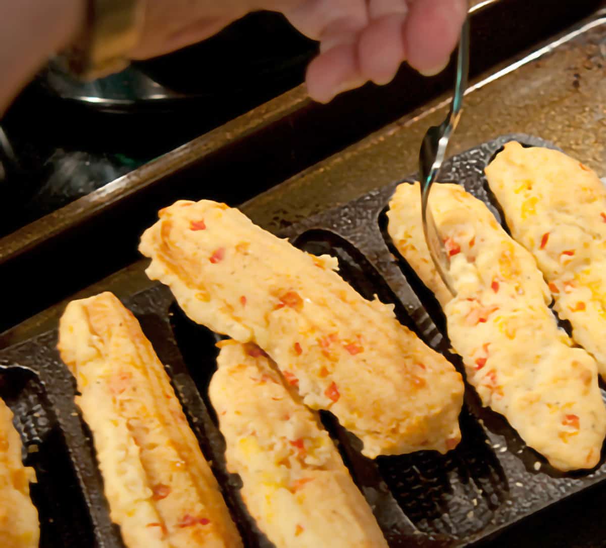 Using a fork to gently loosen the cooked corn sticks from the pan.