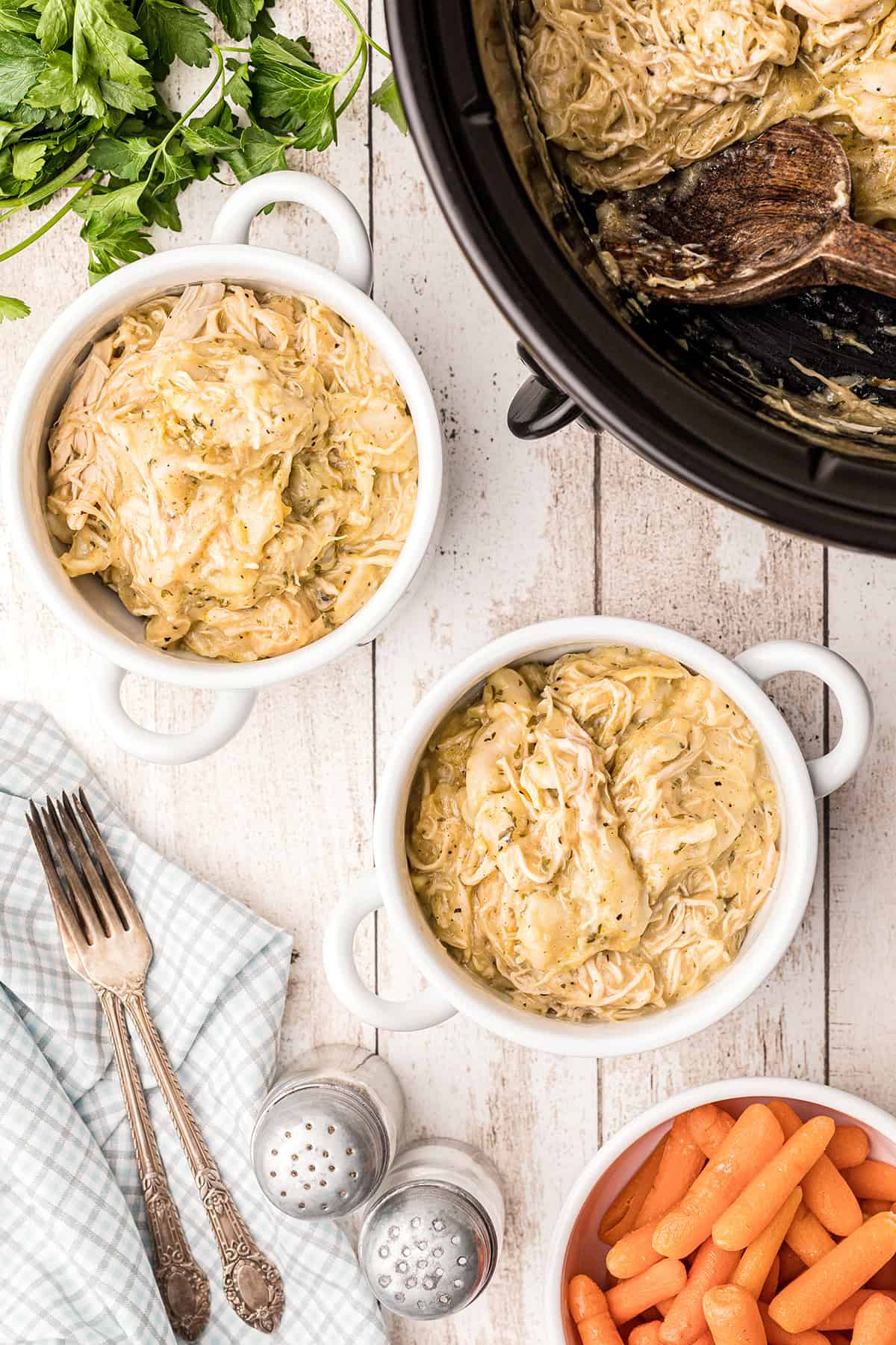 Two servings of chicken and dumplings in white bowls with a slow cooker in the background.