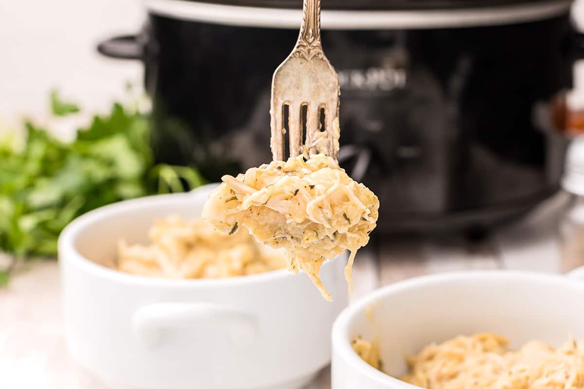 A forkful of slow cooker chicken and dumplings with a slow cooker in the background.