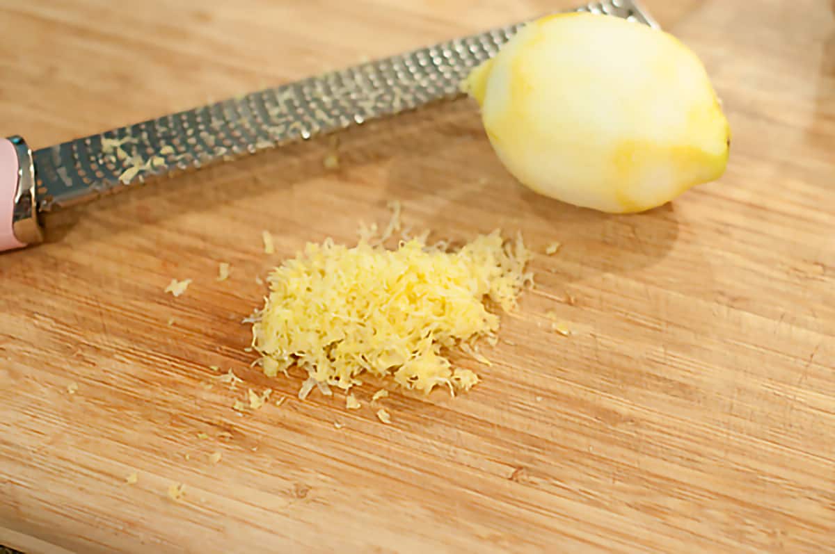 A lemon with its zest and a grater on a cutting board.