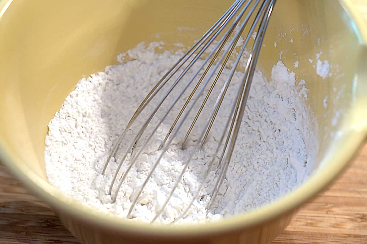 A yellow mixing bowl containing dry ingredients and a whisk.