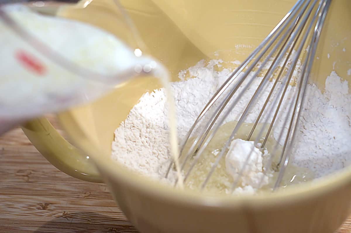 Pouring wet ingredients into dry ingredients in a mixing bowl.