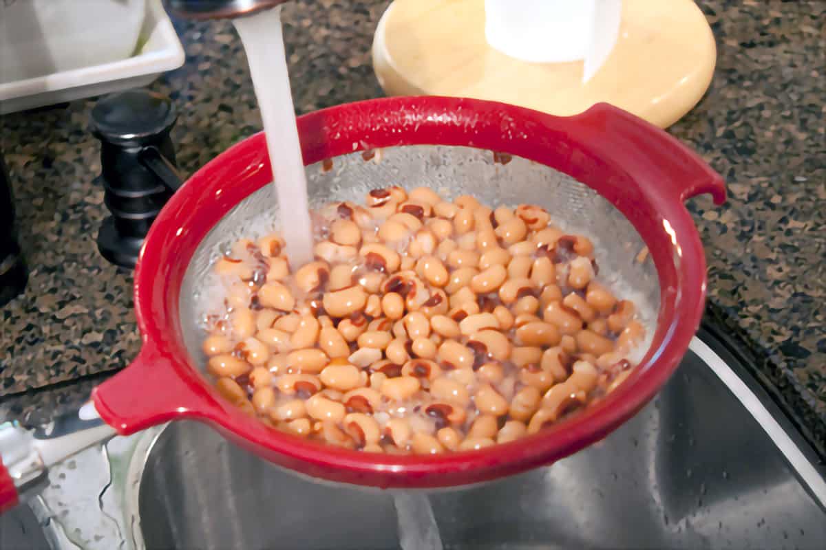 Canned black eyed peas being rinsed in a colander under running water.