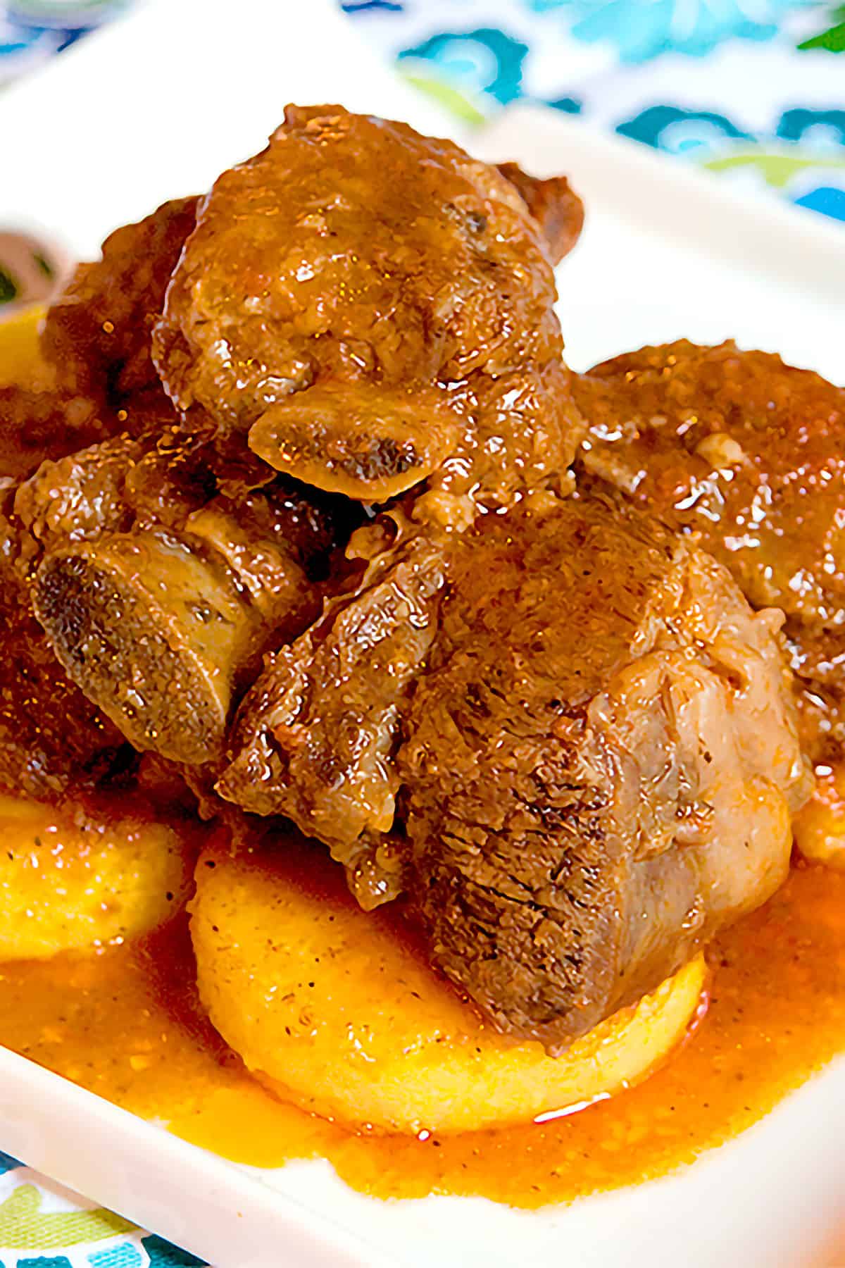 Finished beef short ribs over polenta on a serving plate.