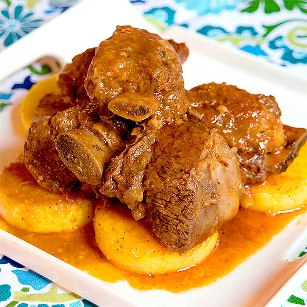 Braised short ribs over polenta on a serving plate.