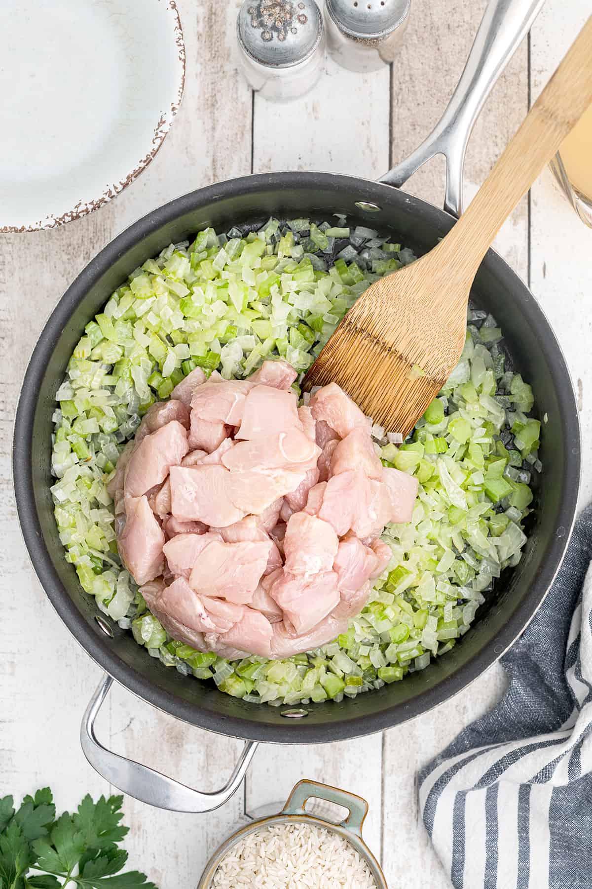 Chicken added to vegetables and butter in a skillet.