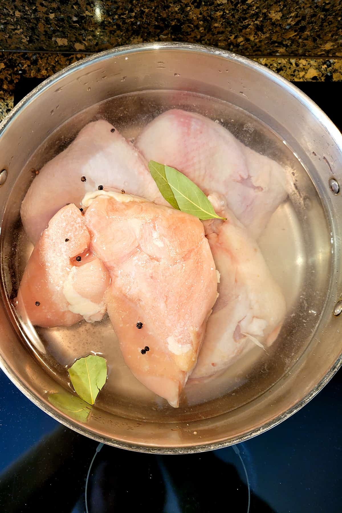 Chicken and by leaves in a deep pot covered in water.