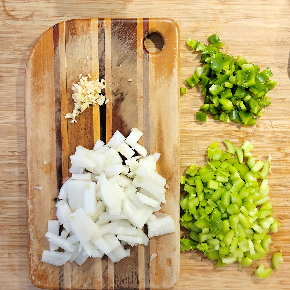 Chopped garlic, onion, bell pepper, and celery on a cutting board.