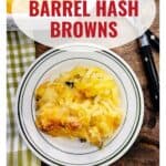 Plate of cheesy hash browns on a table with a fork and knife, labeled Cracker Barrel Hash Browns.
