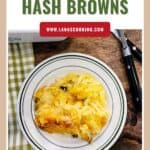 A plate of hash browns on a wooden table with a fork, knife, and green-checkered napkin nearby.