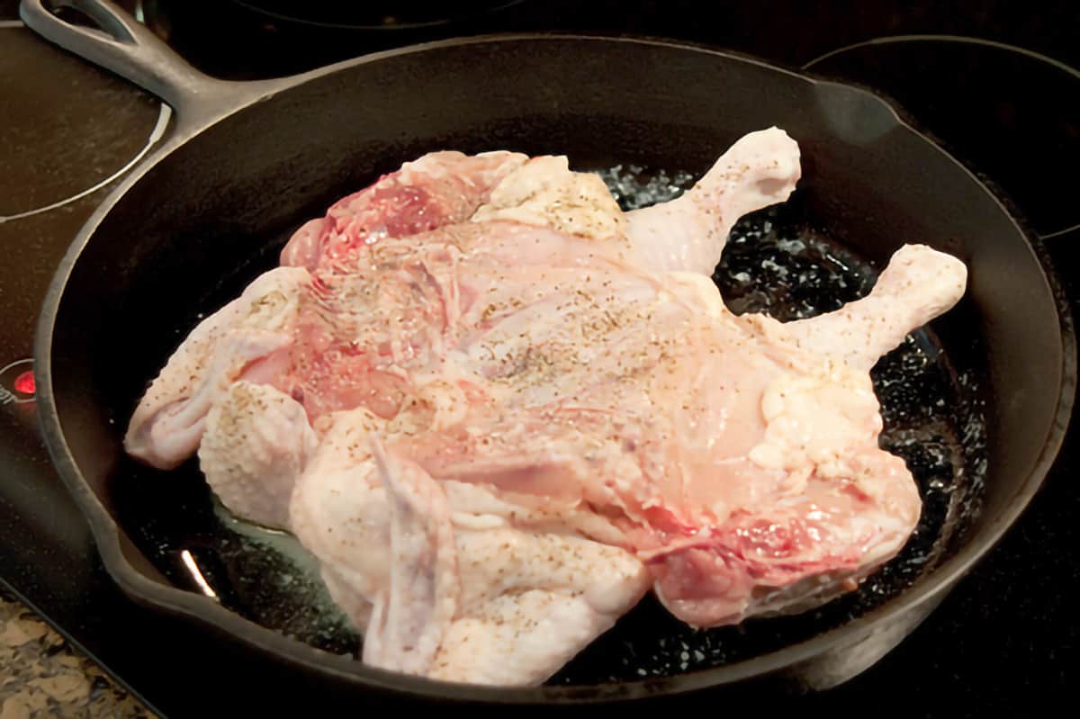 A whole spatchcocked chicken in a large cast iron skillet.