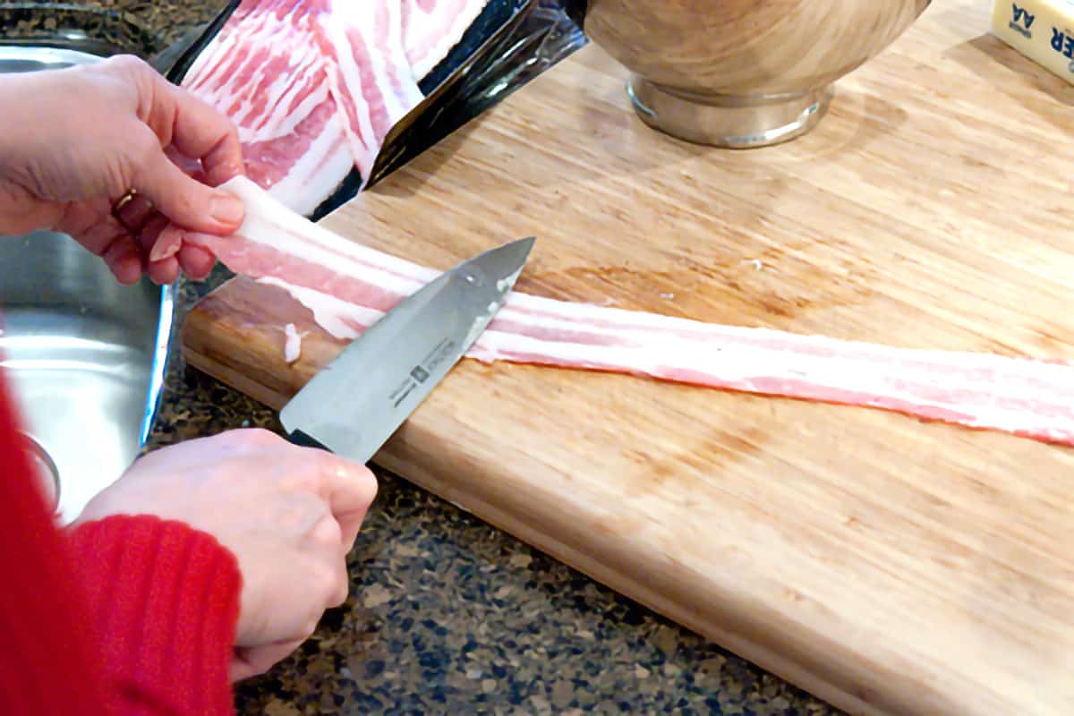 A slice of bacon being stretched out on a cutting board.