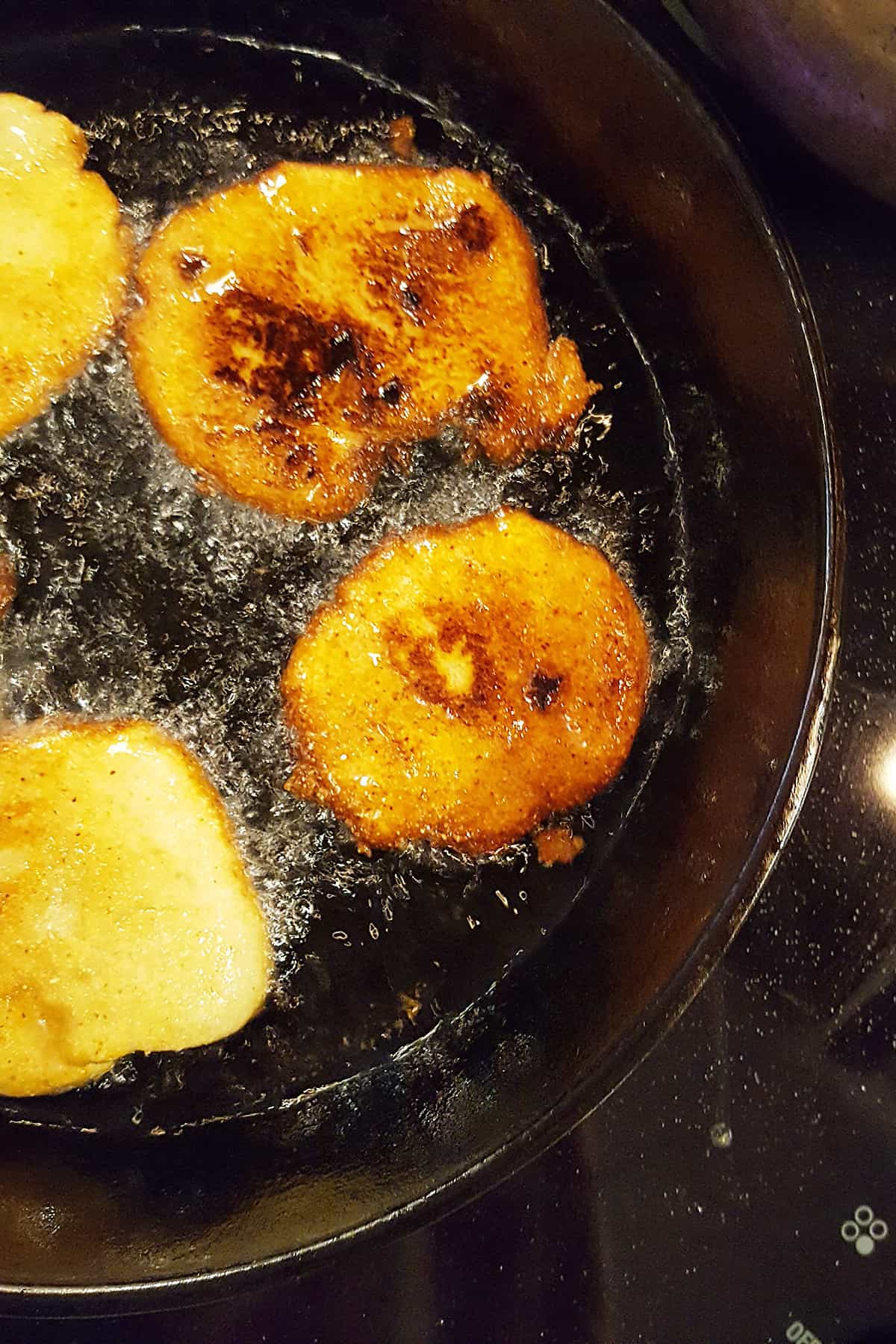 Cornmeal patties in a cast iron skillet after browning on the second ide.