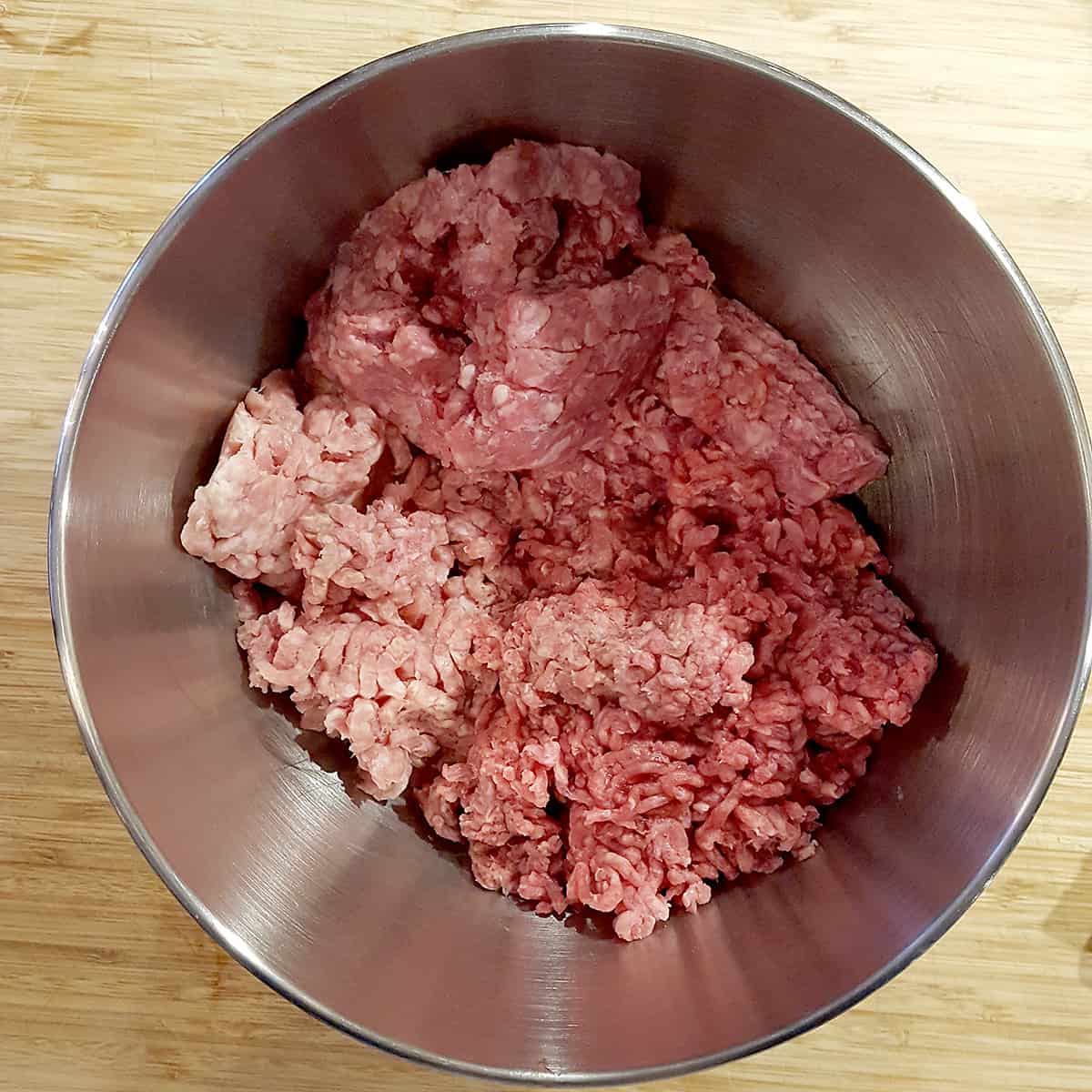 Ground beef, ground pork, and ground veal in the bowl of a stand mixer.