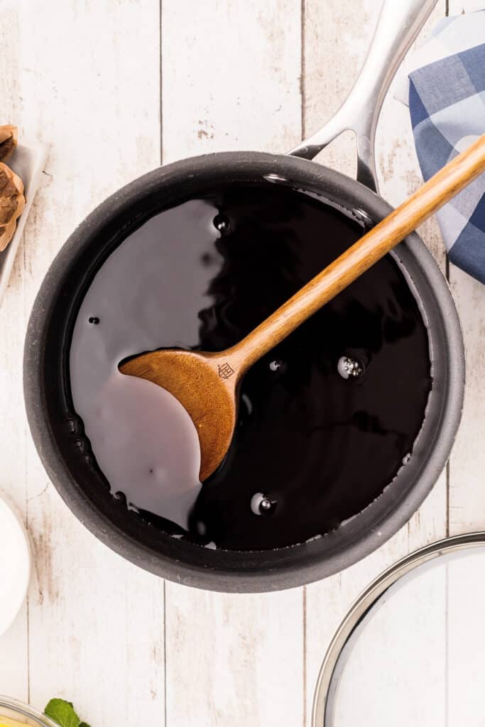 Wooden spoon stirring tea and sugar in a pot.