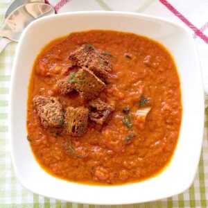 A bowl of tomato fennel soup with croutons on top.