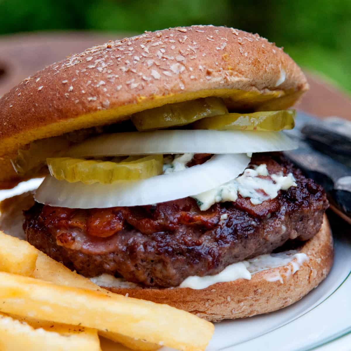 Bacon cheeseburger on a bun with fries on a plate.