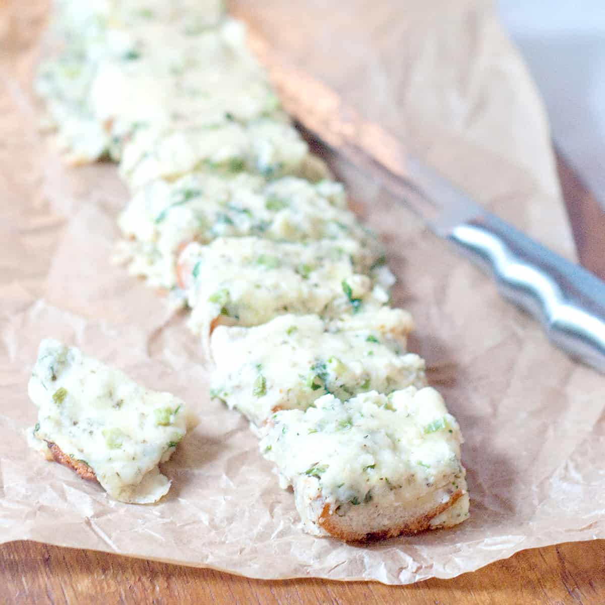 Cheesy onion and herb bread on a cutting board with a bread knife on the side.