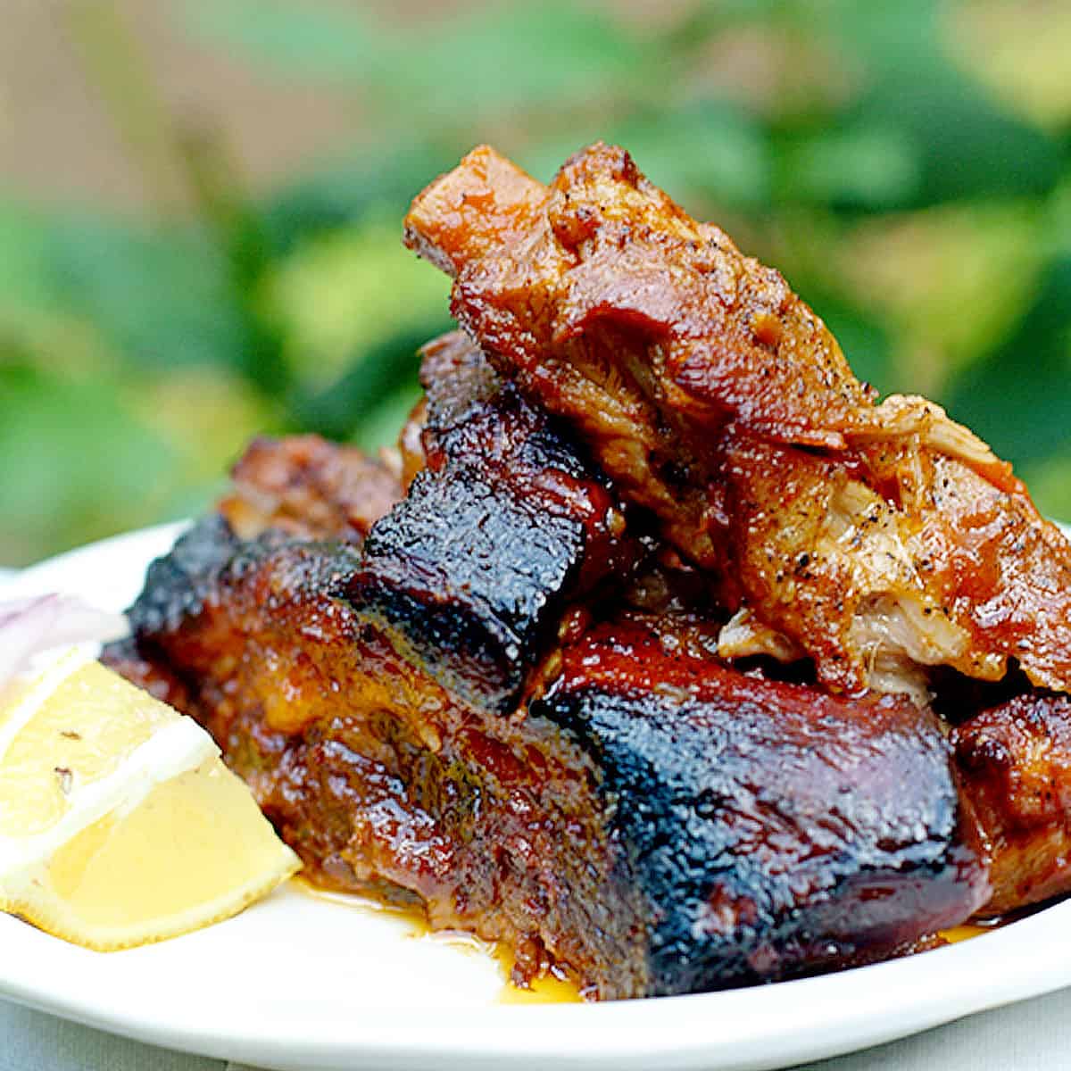 Barbecued ribs stacked on a white plate.