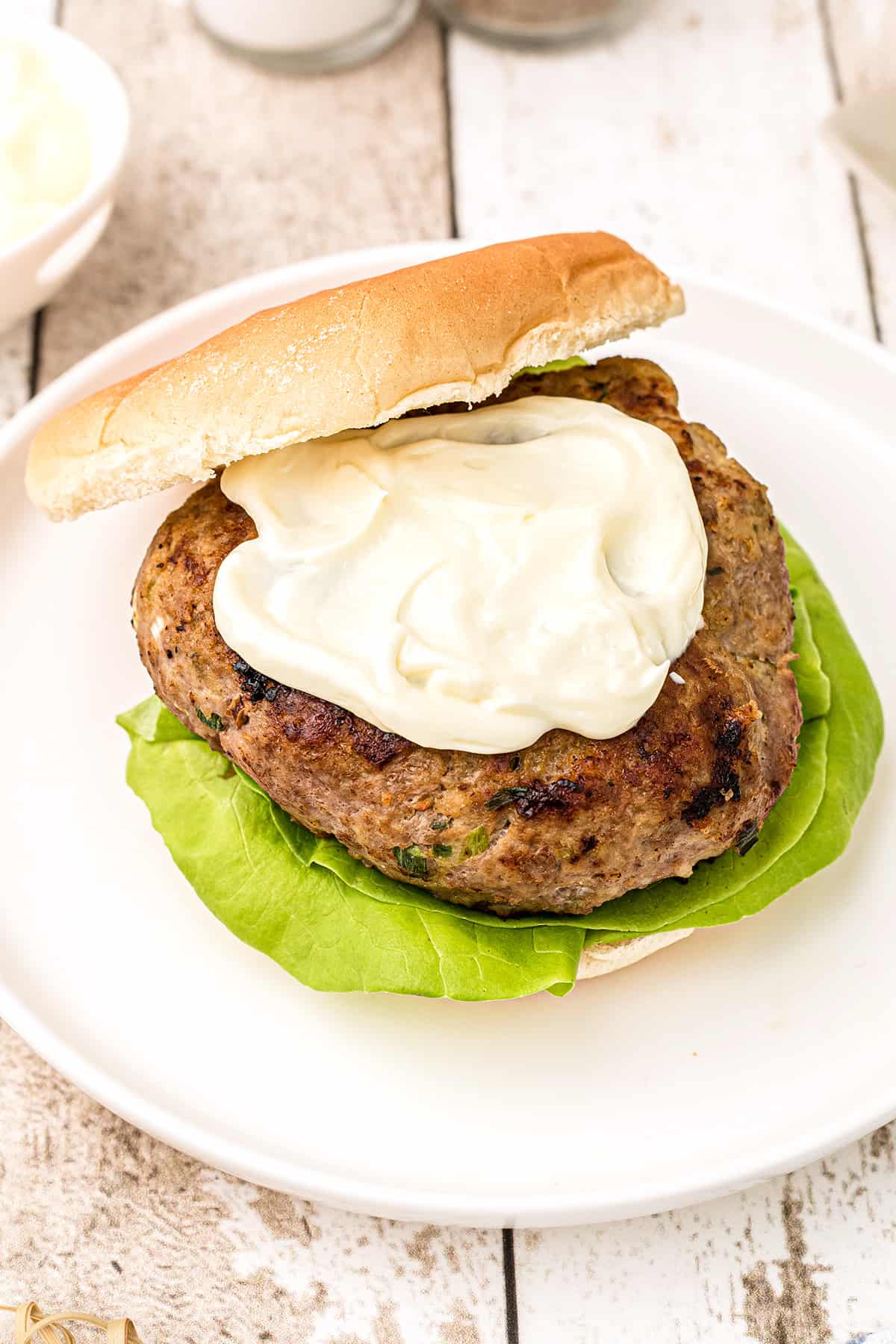 A turkey burger patty on a bun atop a white plate topped with mayonnaise.