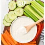 Bowl of blue cheese dip with sliced cucumber, celery, carrots, and red bell pepper on a wooden board.