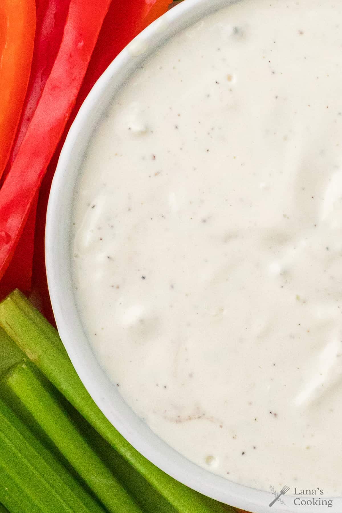 Close-up of blue cheese dip in a white bowl with celery and red bell pepper slices beside it.