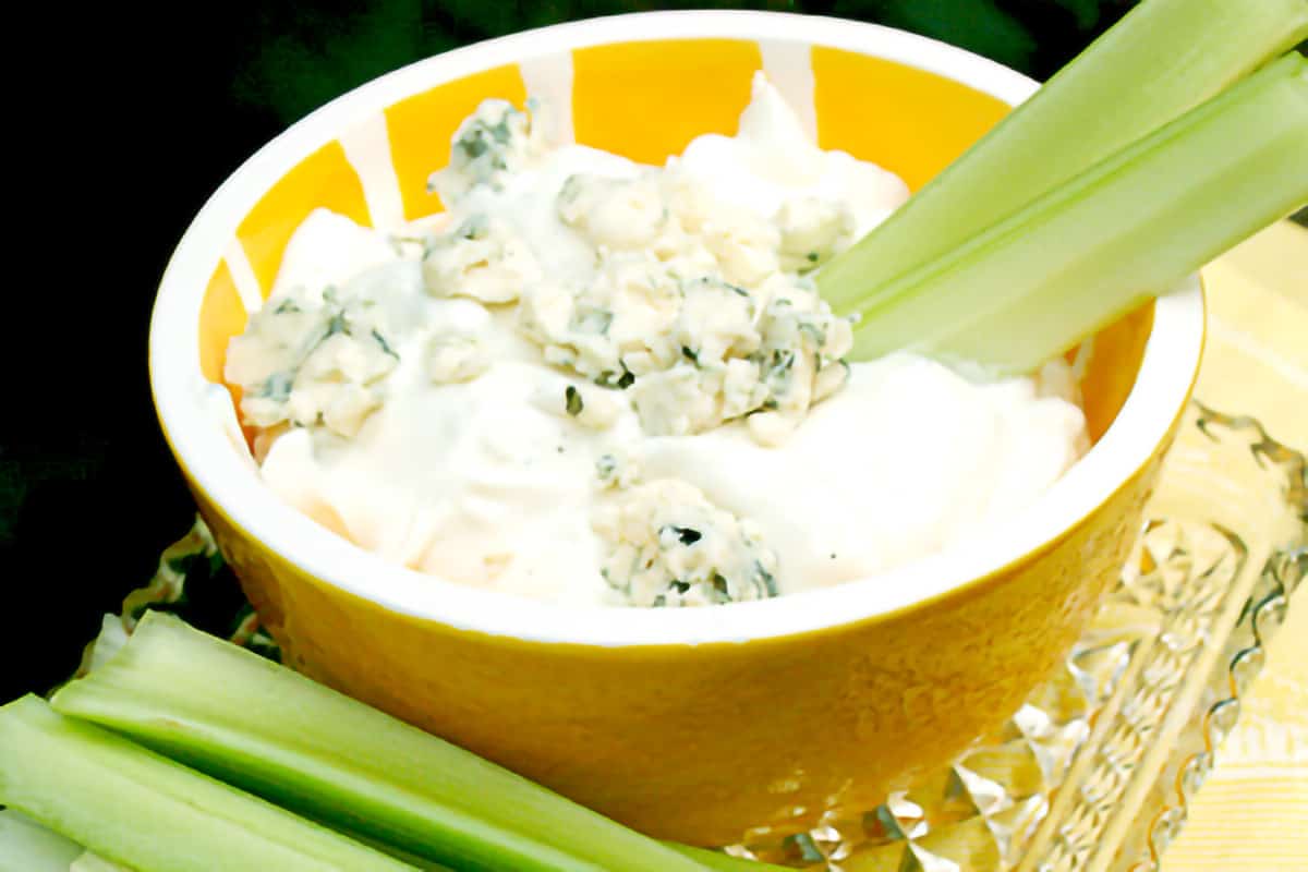 Blue cheese dip in a decorative bowl with celery sticks alongside.