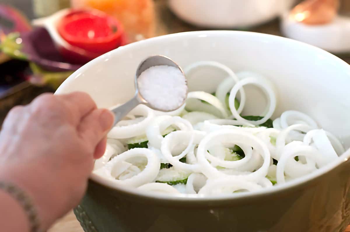 Adding salt to a bowl with cucumber and onion slices.