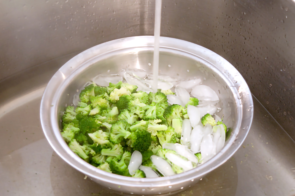 Broccoli and ice in a colander with water running over.