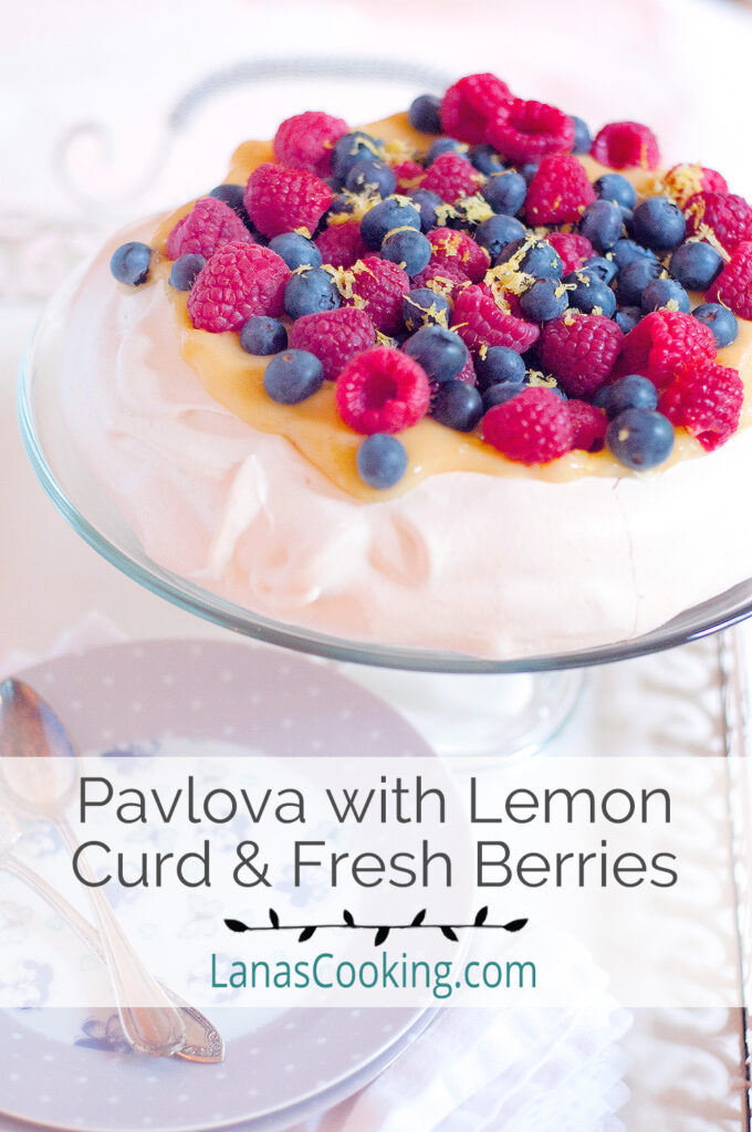 Pavlova topped with lemon curd and fresh berries on a cake stand.
