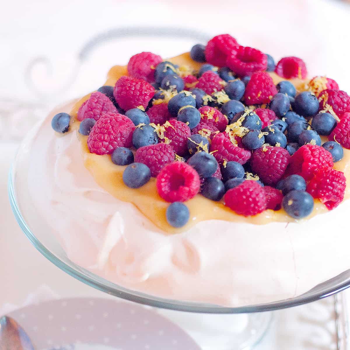 Pavlova topped with lemon curd and fresh berries on a cake stand.