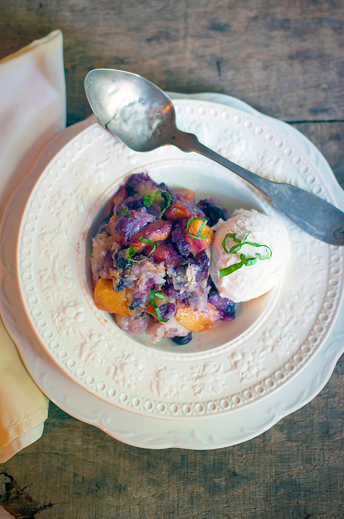 A serving of peach blueberry basil cobbler in a bowl with ice cream.