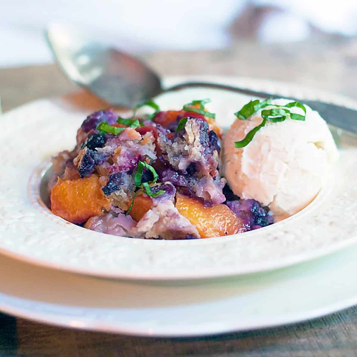 A serving of peach blueberry basil cobbler in a bowl with ice cream.