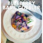 A plate of peach blueberry basil cobbler with ice cream, garnished with basil, on a wooden table.