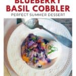 A plate with peach blueberry basil cobbler and ice cream, garnished with fresh basil, on white dishes.