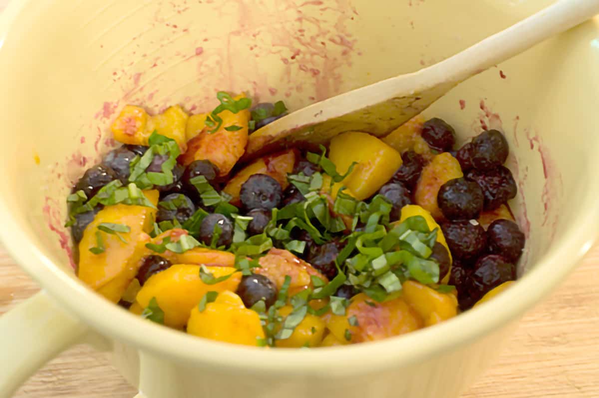 Adding fresh basil to fruit in a bowl.