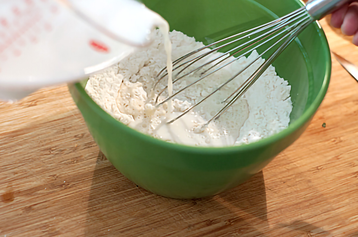 Whisking wet ingredients into dry ingredients in a mixing bowl.
