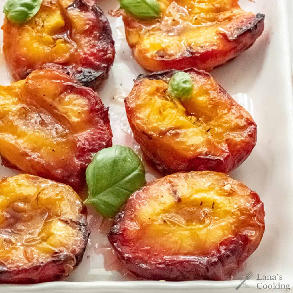Grilled peach halves on a white plate, topped with fresh basil leaves and a glistening glaze.