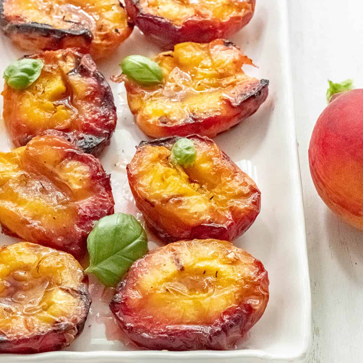 Grilled peach halves on a white serving plate.