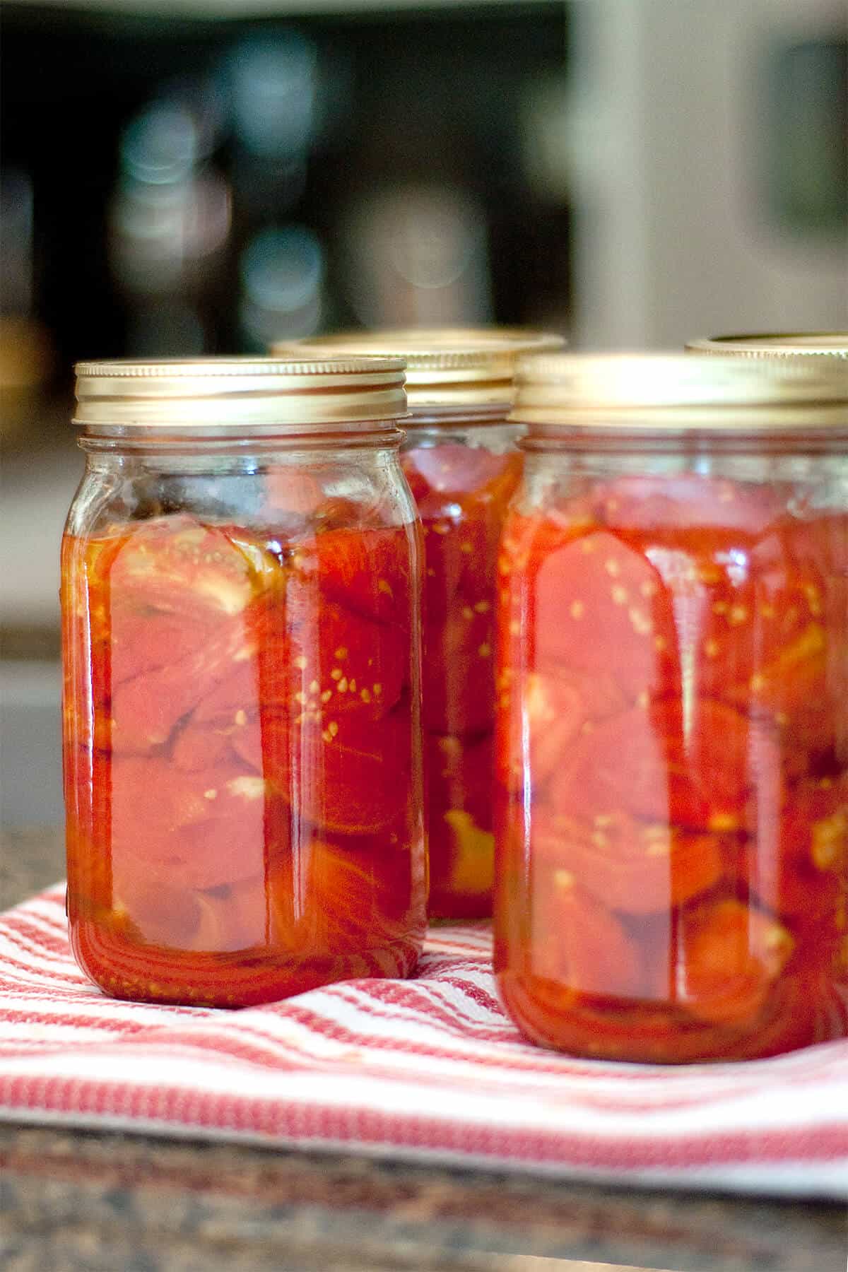 Jars of home canned tomatoes on a kitchen towel.