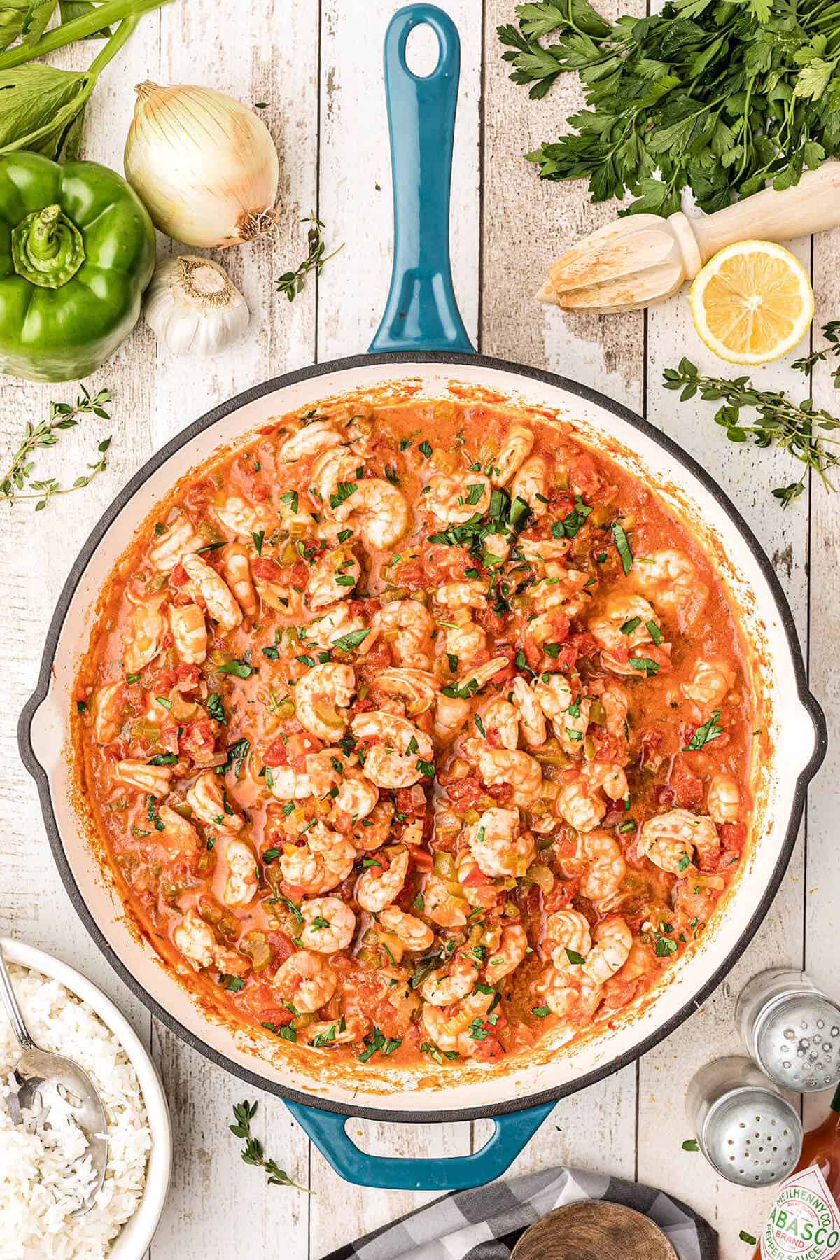 A skillet filled with shrimp creole and a bowl of steam rice alongside.