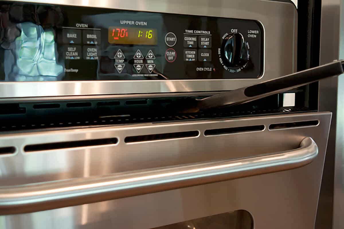 Oven door propped open with a pair of tongs.