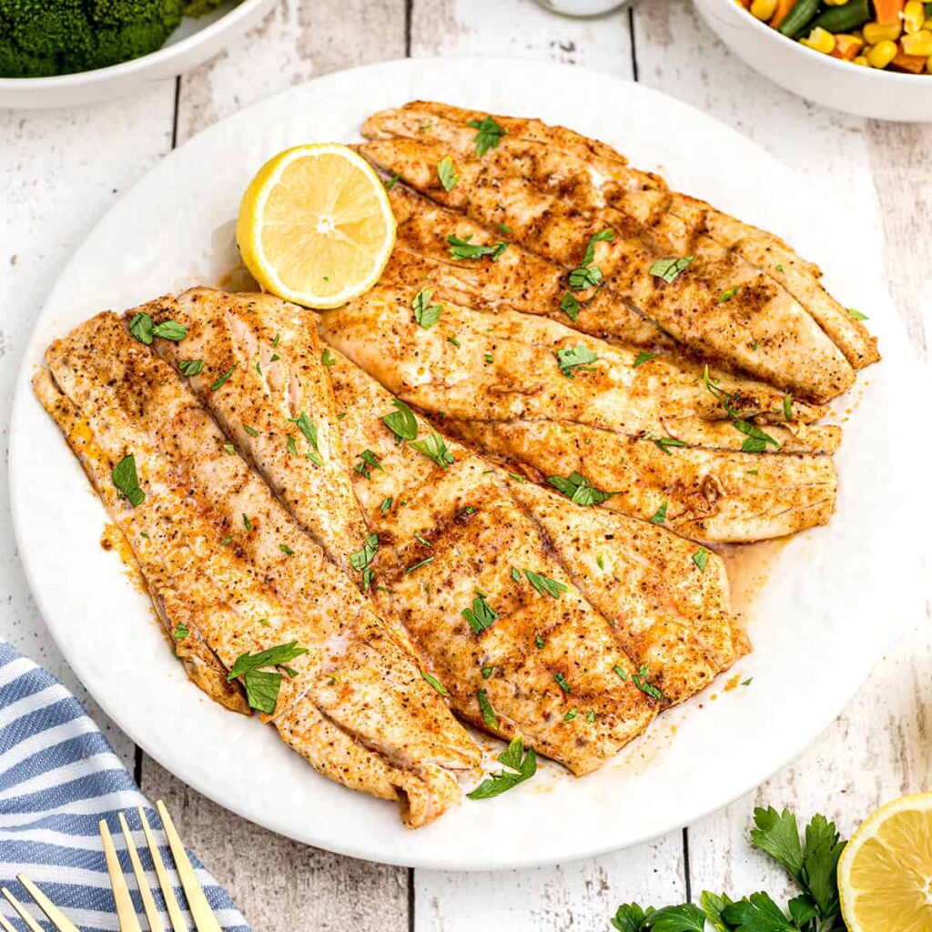 Grilled fish with lemon and parsley on a serving plate.