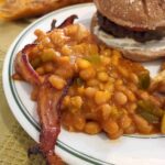 Baked beans and bacon on a plate with a hamburger.