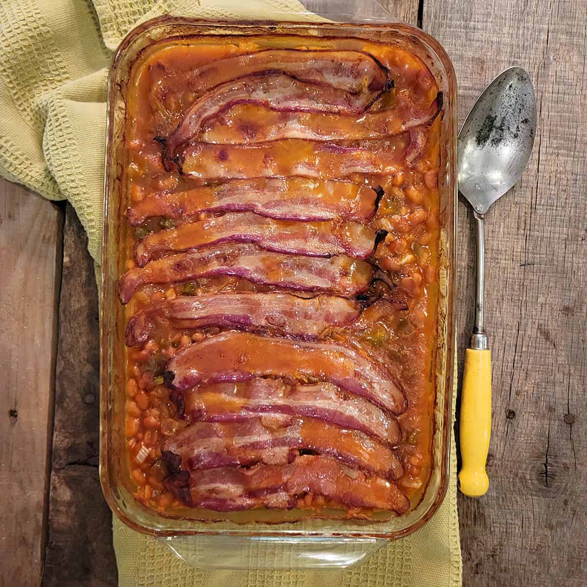 Cooked baked beans in a casserole dish on a wooden board.